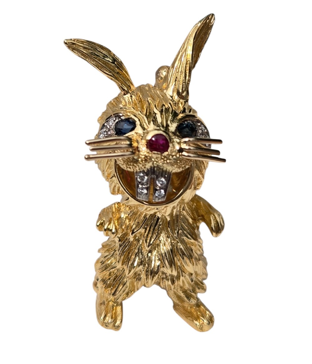 An 18ct yellow gold rabbit brooch showcasing textured fur detailing, a ruby nose, diamond-set teeth, and sapphire eyes. View IX