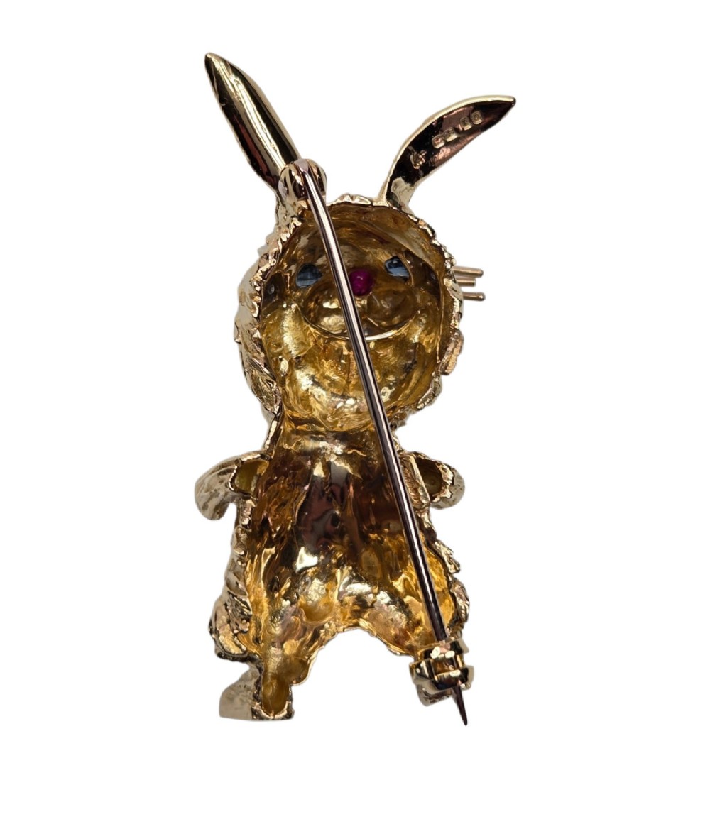 An 18ct yellow gold rabbit brooch showcasing textured fur detailing, a ruby nose, diamond-set teeth, and sapphire eyes. View XI
