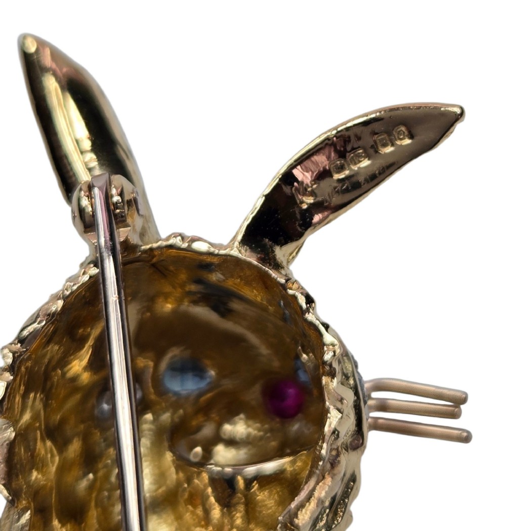 An 18ct yellow gold rabbit brooch showcasing textured fur detailing, a ruby nose, diamond-set teeth, and sapphire eyes. View XII