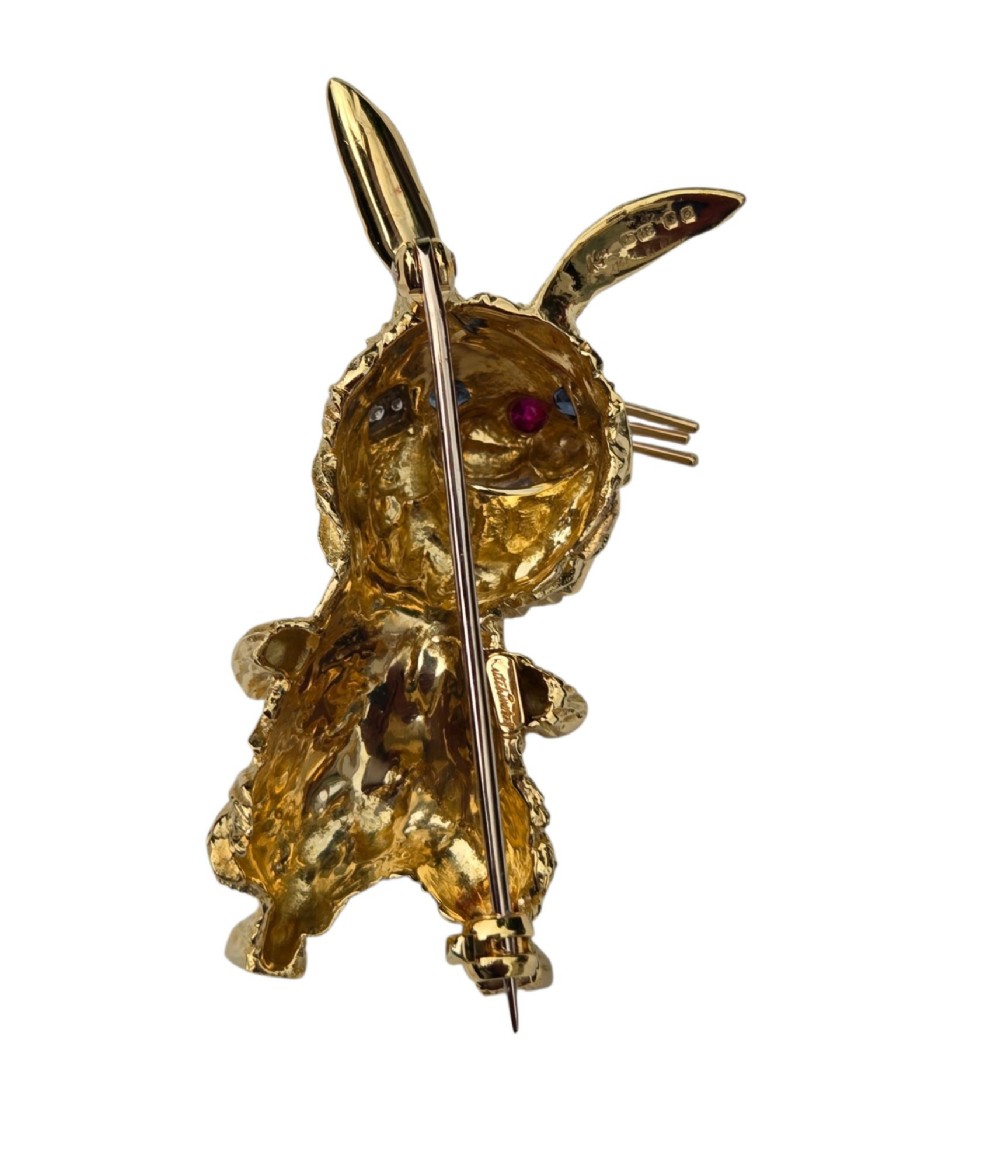 An 18ct yellow gold rabbit brooch showcasing textured fur detailing, a ruby nose, diamond-set teeth, and sapphire eyes. View XIII
