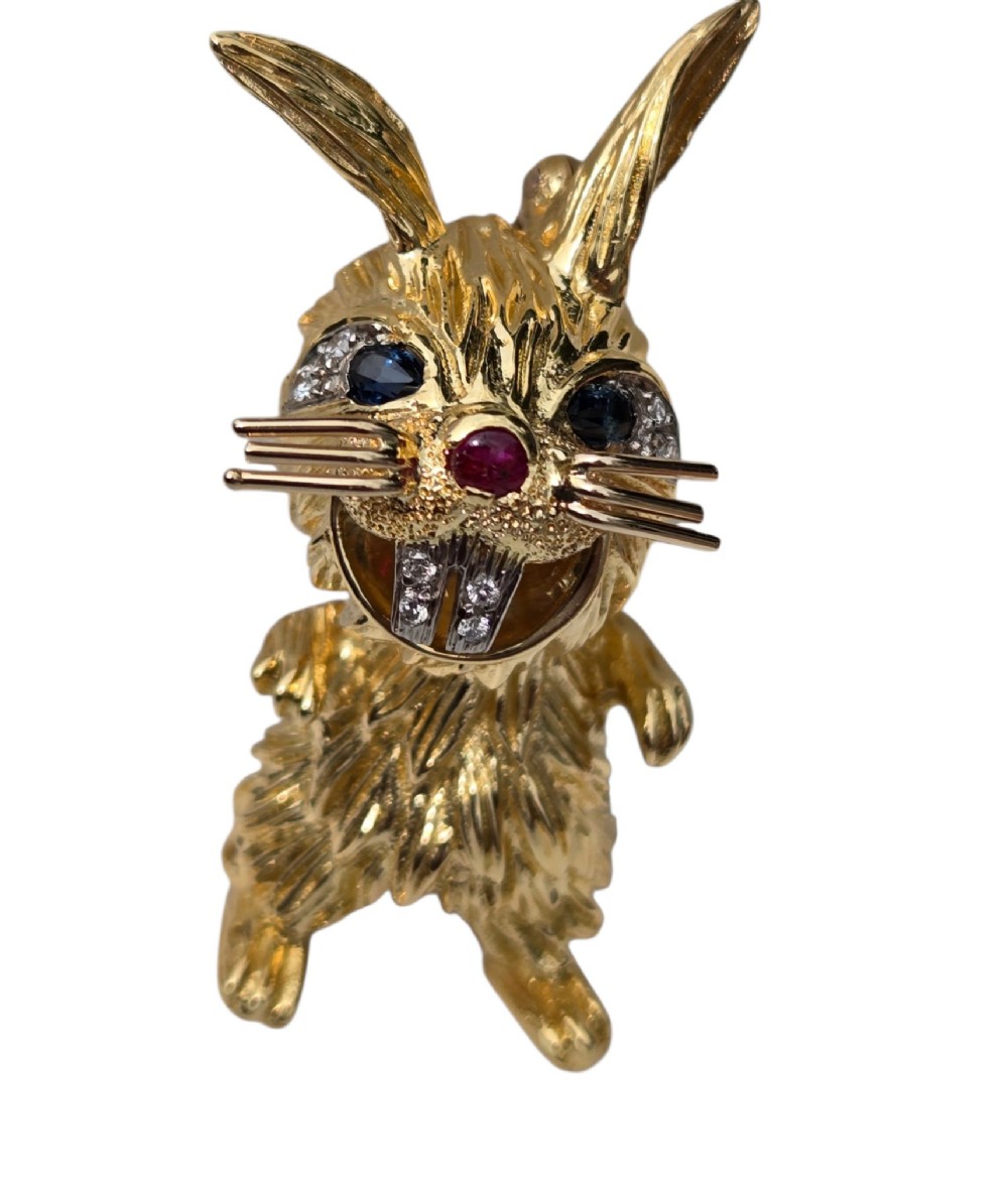 An 18ct yellow gold rabbit brooch showcasing textured fur detailing, a ruby nose, diamond-set teeth, and sapphire eyes. View XIV