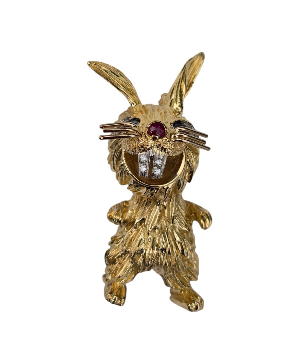 An 18ct yellow gold rabbit brooch showcasing textured fur detailing, a ruby nose, diamond-set teeth, and sapphire eyes. View XV