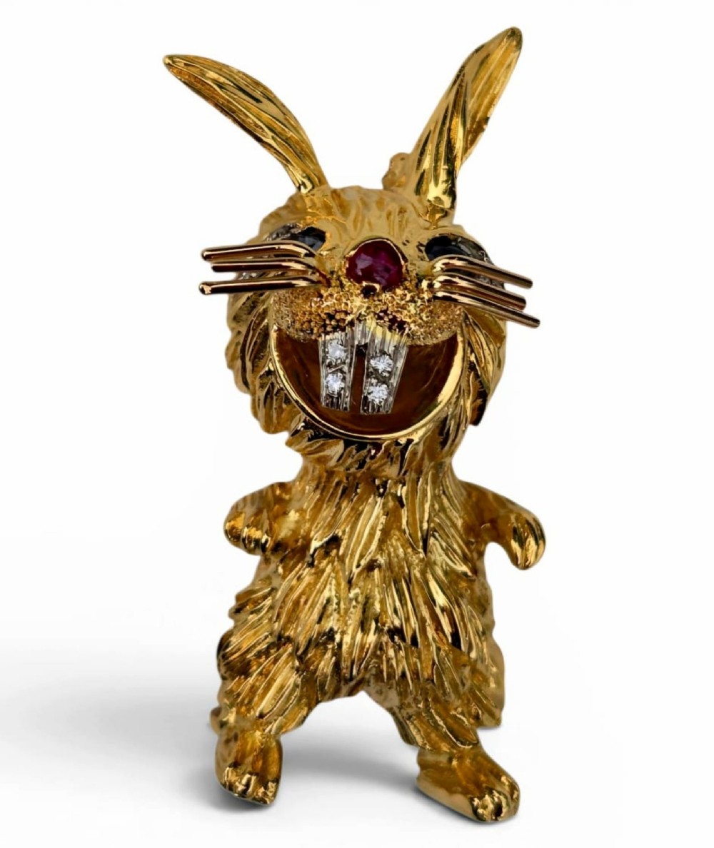 An 18ct yellow gold rabbit brooch showcasing textured fur detailing, a ruby nose, diamond-set teeth, and sapphire eyes.