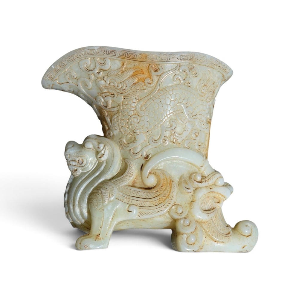 A carved pale celadon nephrite jade rhyton cup featuring relief dragon and mythical beast motifs with subtle russet inclusions. View II