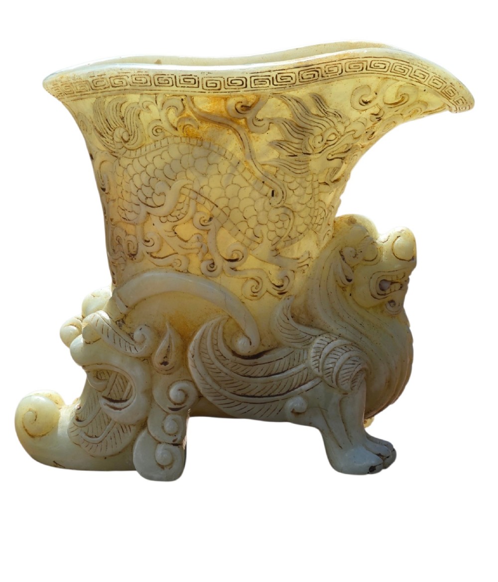 A carved pale celadon nephrite jade rhyton cup featuring relief dragon and mythical beast motifs with subtle russet inclusions. View III