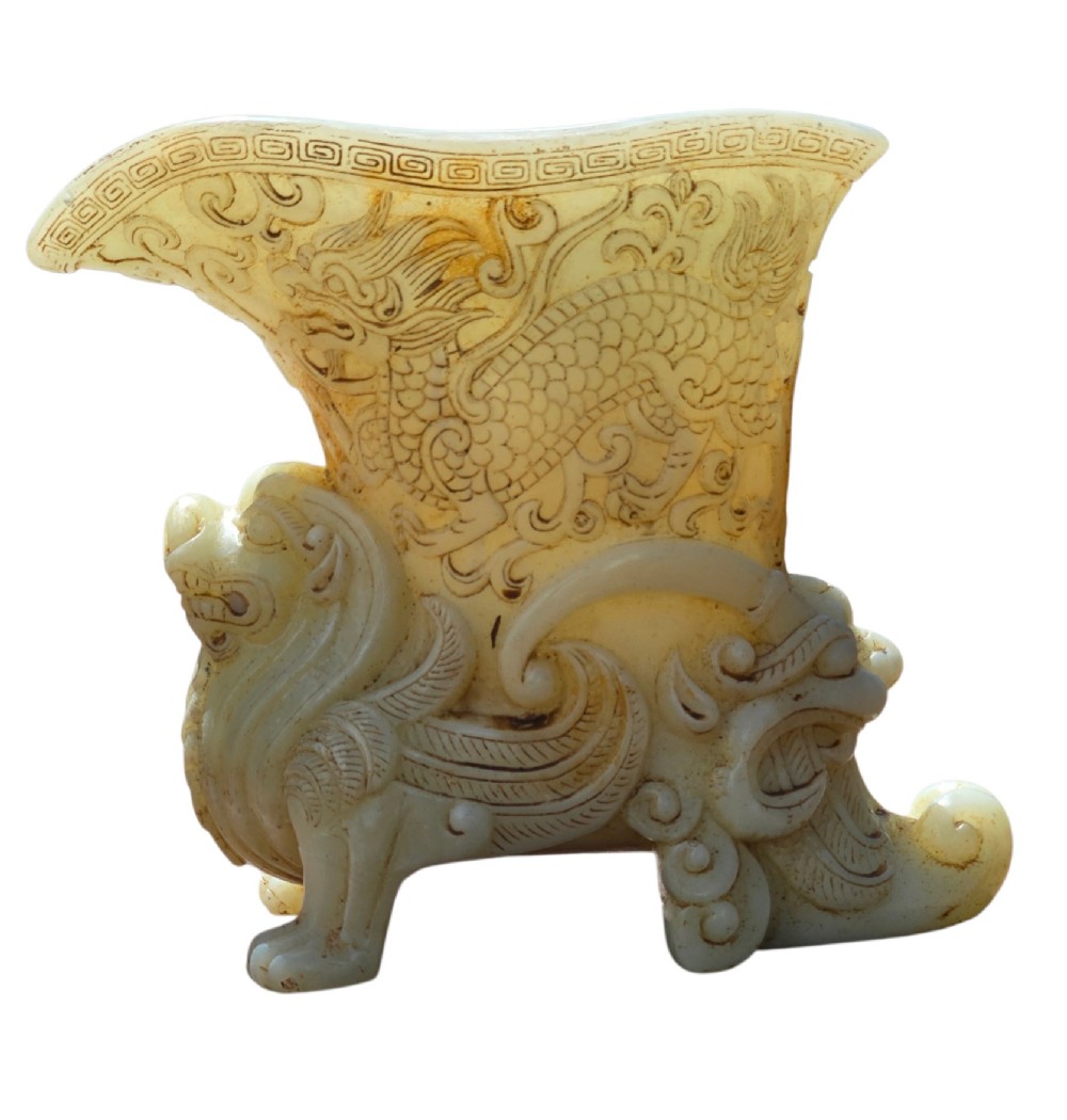 A carved pale celadon nephrite jade rhyton cup featuring relief dragon and mythical beast motifs with subtle russet inclusions. View IV