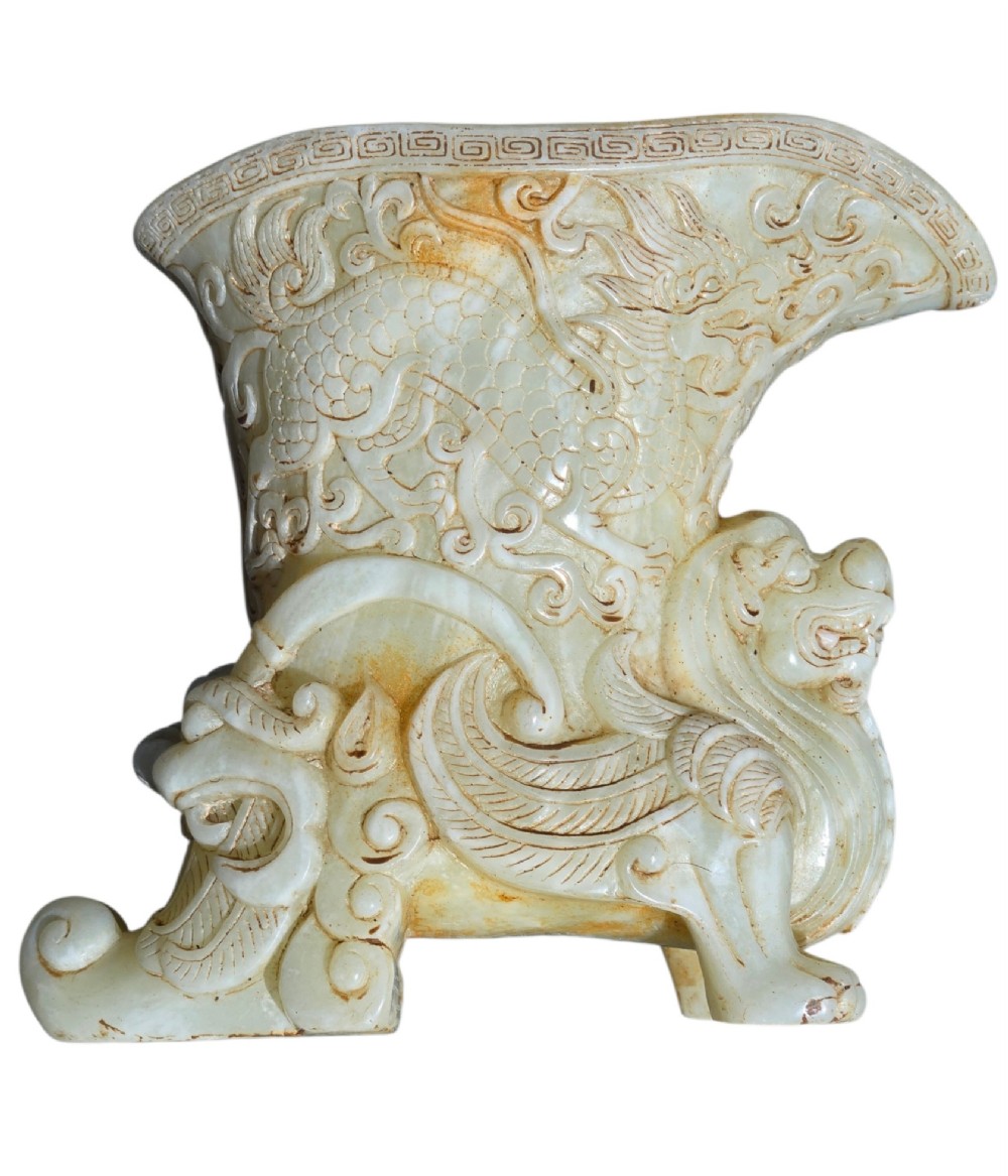 A carved pale celadon nephrite jade rhyton cup featuring relief dragon and mythical beast motifs with subtle russet inclusions. View V