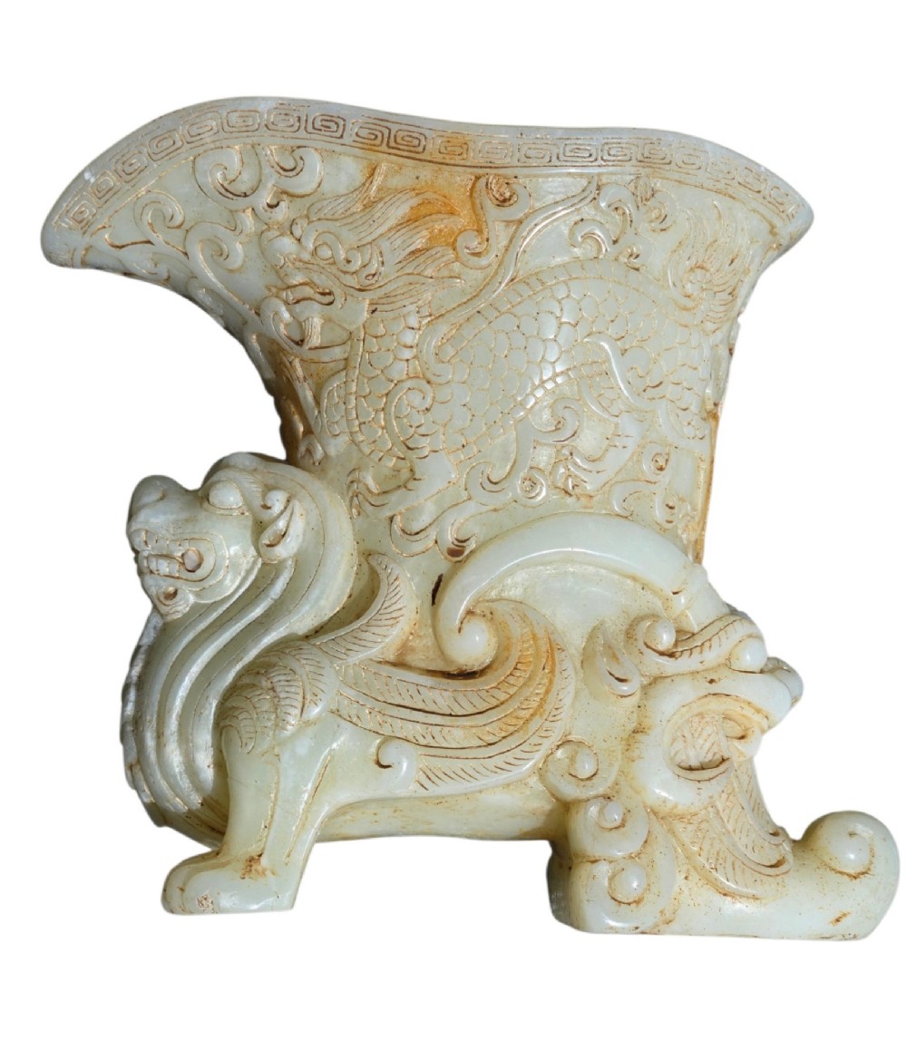 A carved pale celadon nephrite jade rhyton cup featuring relief dragon and mythical beast motifs with subtle russet inclusions. View VI