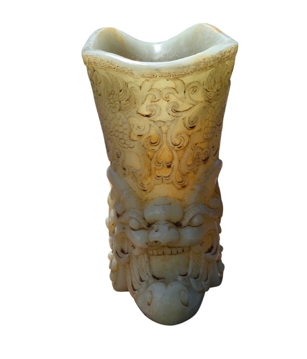 A carved pale celadon nephrite jade rhyton cup featuring relief dragon and mythical beast motifs with subtle russet inclusions. View IX