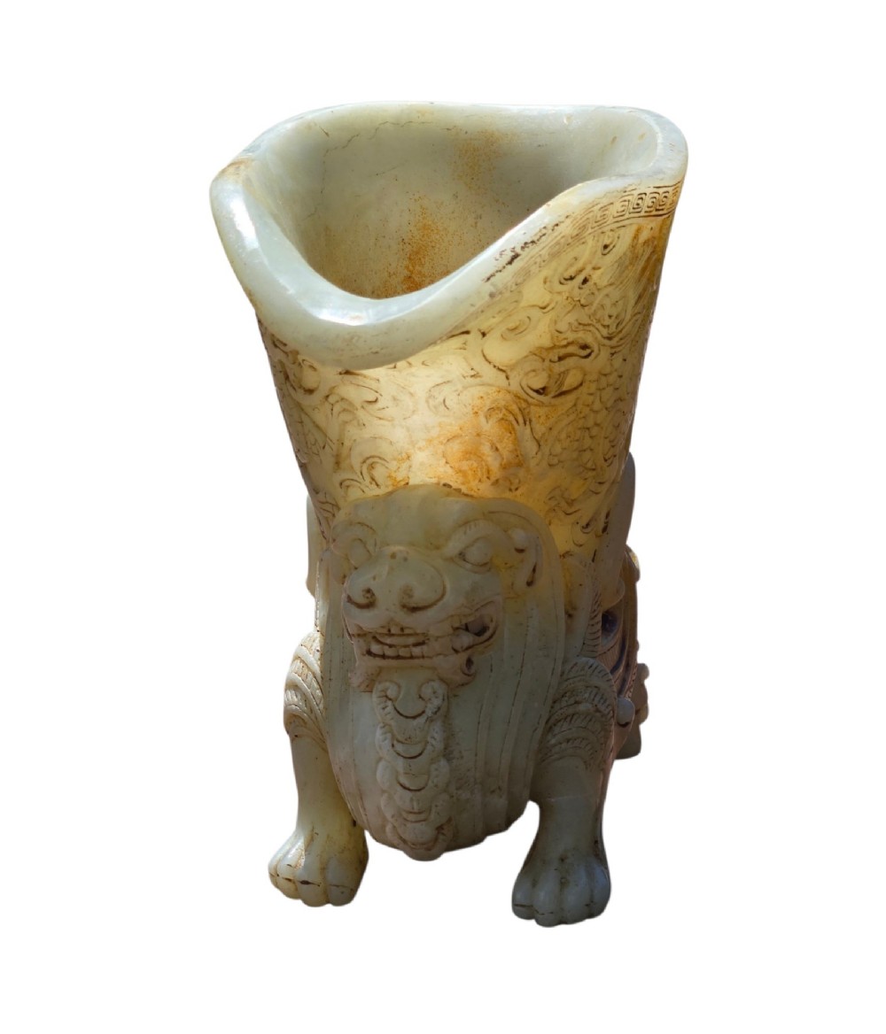 A carved pale celadon nephrite jade rhyton cup featuring relief dragon and mythical beast motifs with subtle russet inclusions. View X