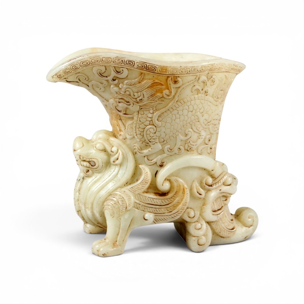 A carved pale celadon nephrite jade rhyton cup featuring relief dragon and mythical beast motifs with subtle russet inclusions. View XII