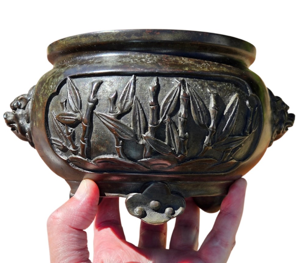 A dark patinated cast bronze incense burner featuring raised relief panels of bamboo and beast mask side handles. View X