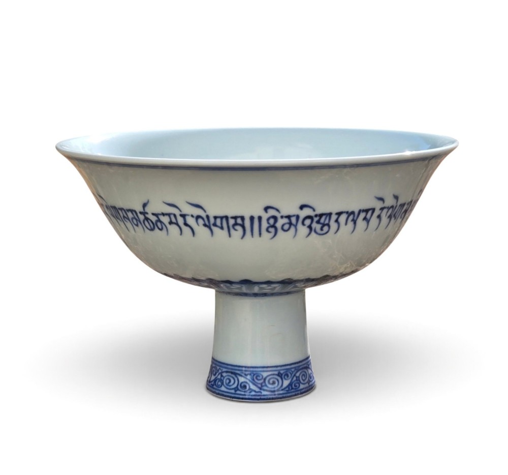 A Chinese blue and white porcelain stem cup featuring Tibetan script around the exterior flared bowl and a hollow cylindrical foot.
