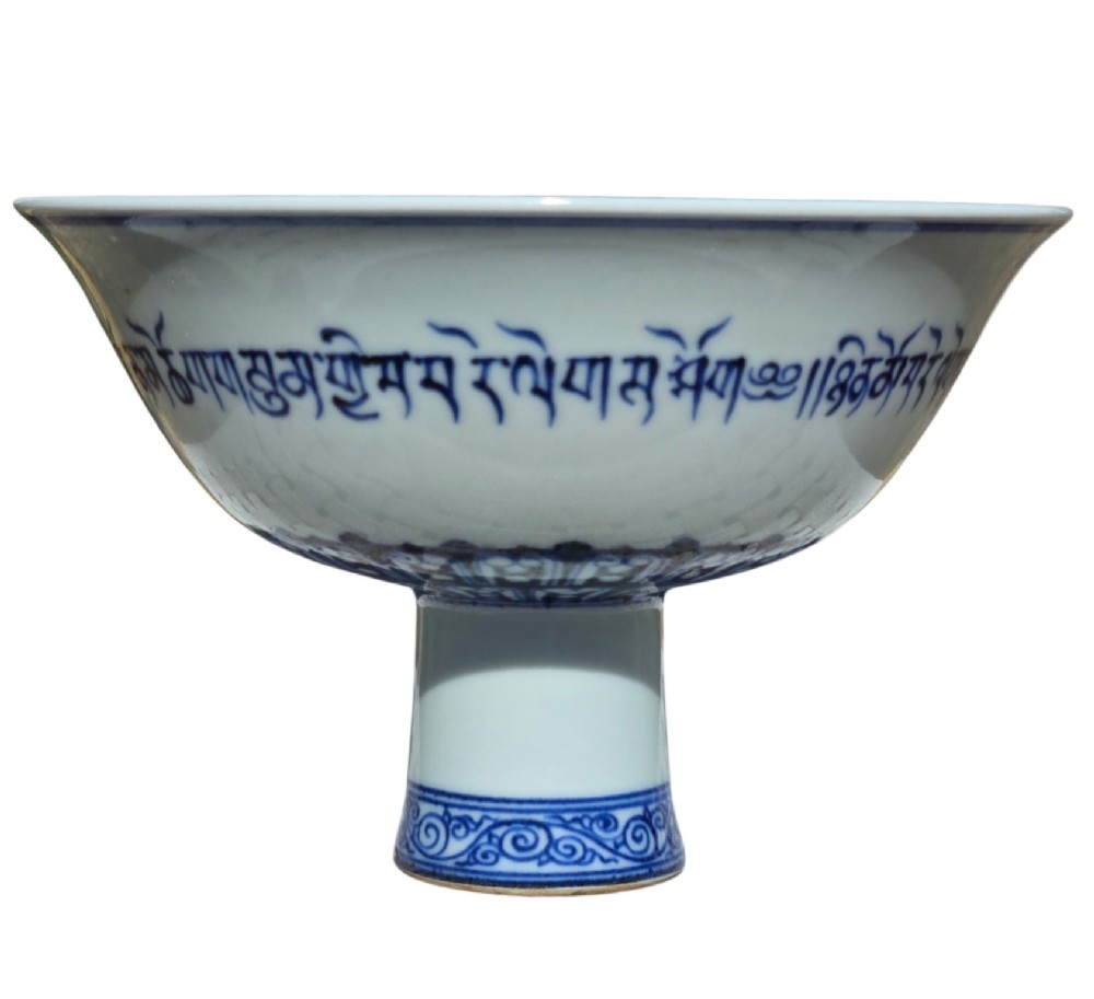 A Chinese blue and white porcelain stem cup featuring Tibetan script around the exterior flared bowl and a hollow cylindrical foot. View II