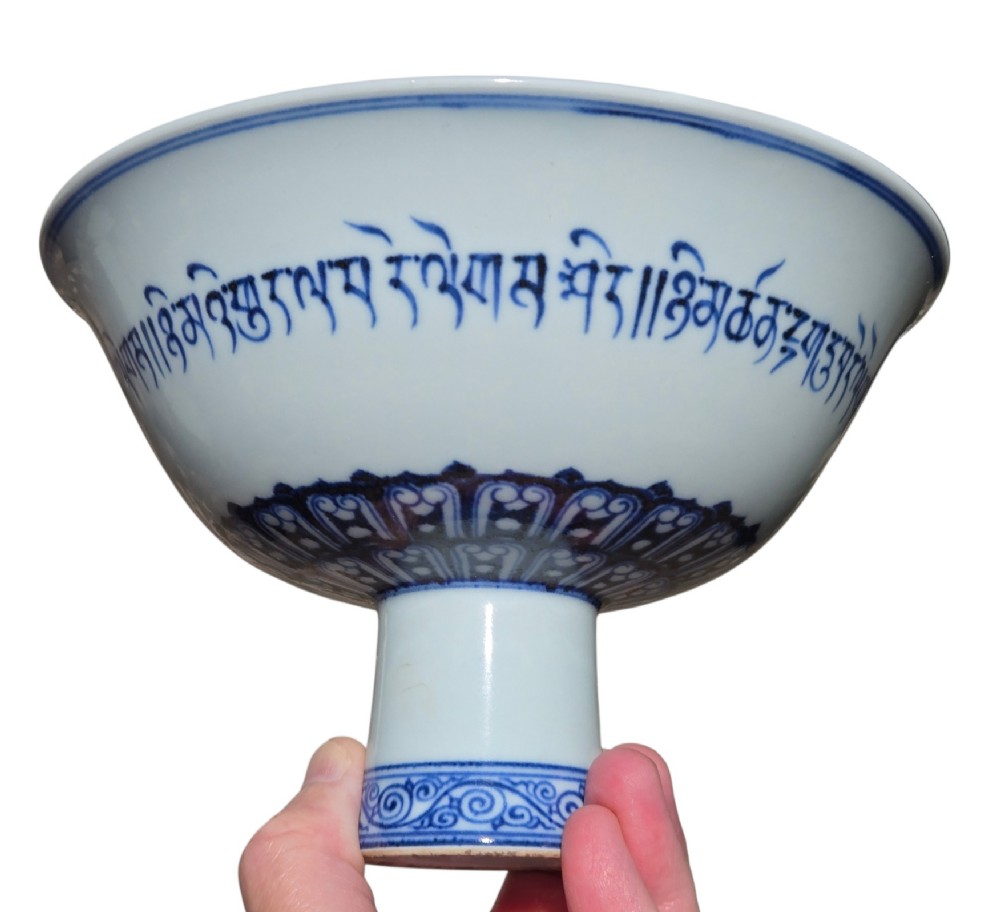 A Chinese blue and white porcelain stem cup featuring Tibetan script around the exterior flared bowl and a hollow cylindrical foot. View V