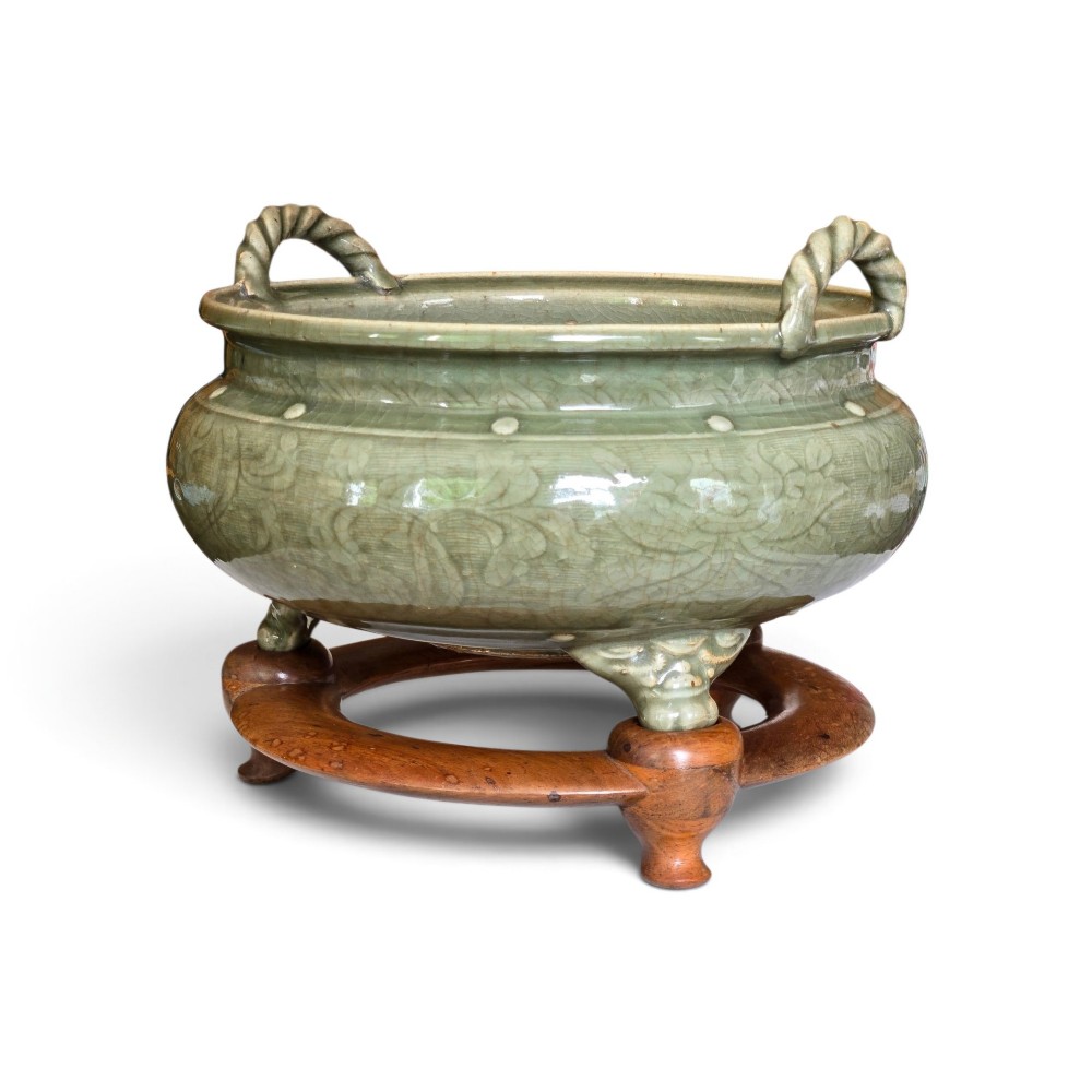 A green glazed Longquan celadon tripod censer with carved floral scrollwork beneath the glaze, twin rope-twist handles, and three mask feet. View III