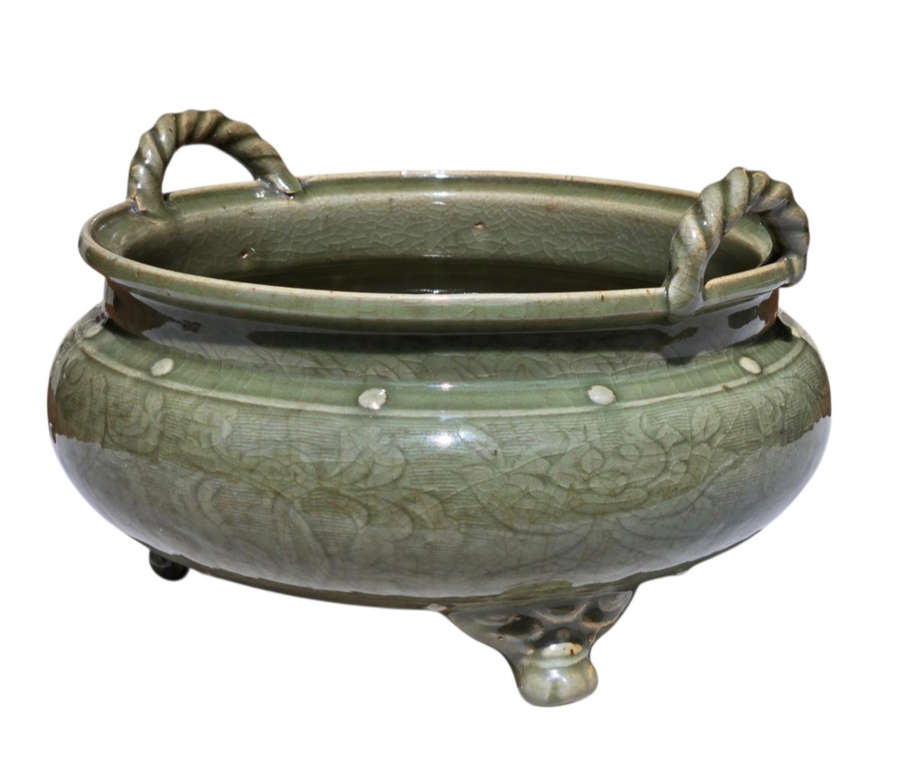 A green glazed Longquan celadon tripod censer with carved floral scrollwork beneath the glaze, twin rope-twist handles, and three mask feet. View V