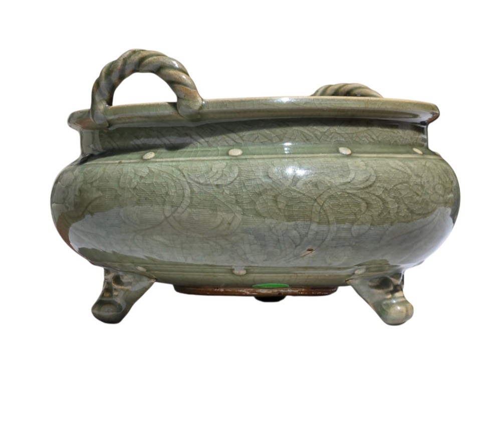 A green glazed Longquan celadon tripod censer with carved floral scrollwork beneath the glaze, twin rope-twist handles, and three mask feet. View VI