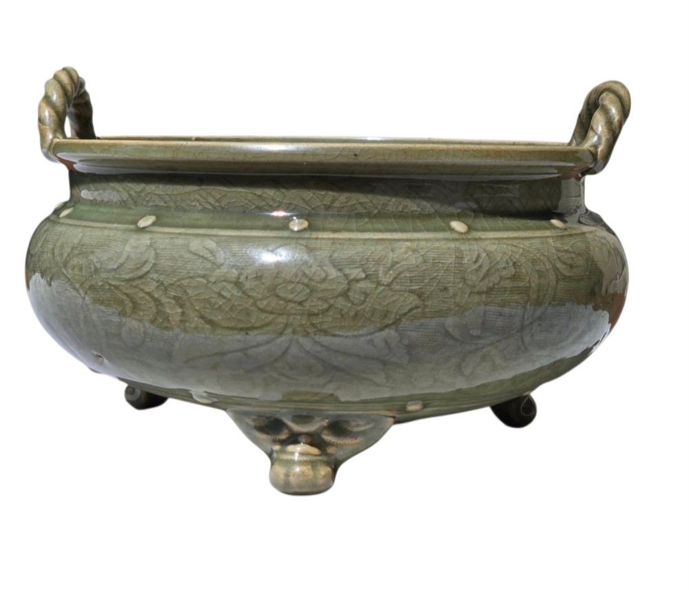 A green glazed Longquan celadon tripod censer with carved floral scrollwork beneath the glaze, twin rope-twist handles, and three mask feet. View IX