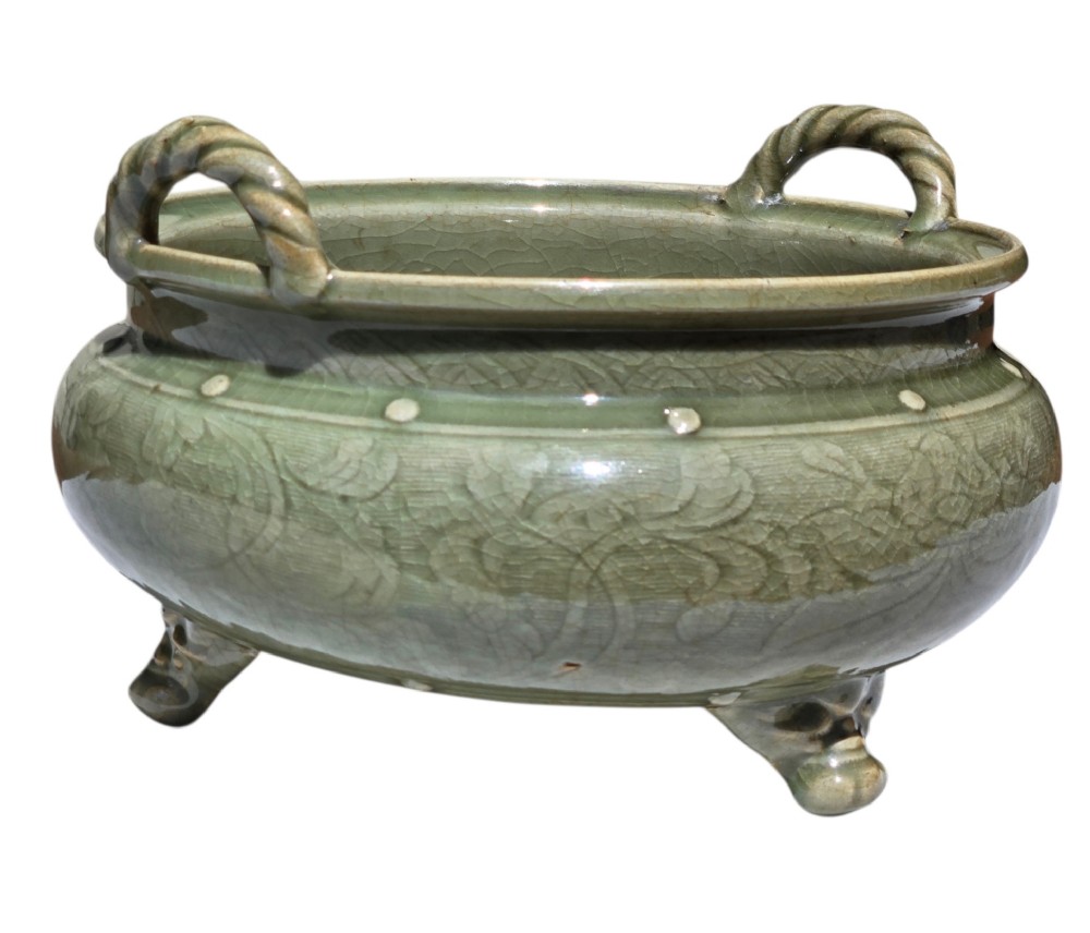 A green glazed Longquan celadon tripod censer with carved floral scrollwork beneath the glaze, twin rope-twist handles, and three mask feet. View XIV