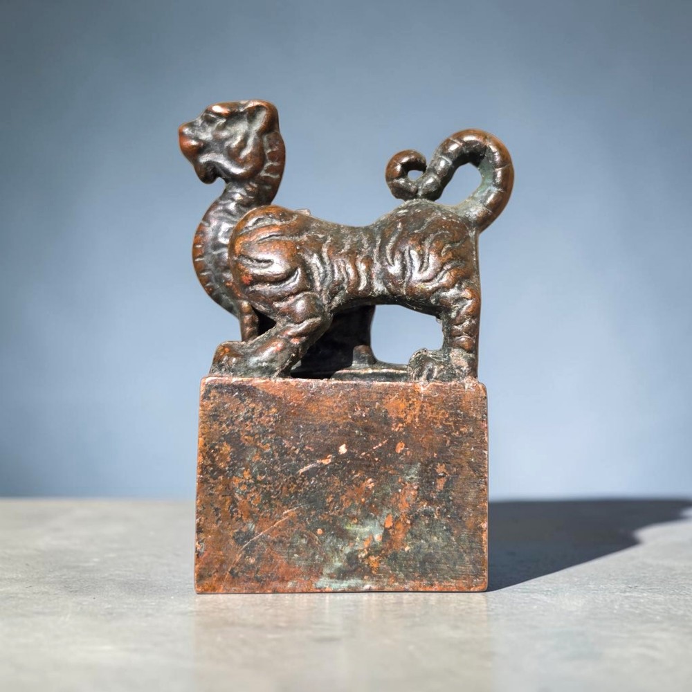 A cast bronze Chinese seal featuring a qilin finial resting atop a square base with reddish brown patination.