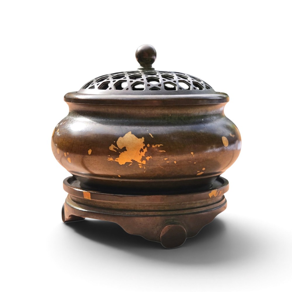 A dark brown bronze circular censer featuring gold splash decoration, a reticulated lattice cover with a spherical finial, and a matching footed bronze stand.