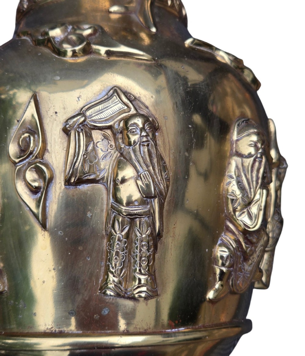 A late 19th-century Chinese brass baluster vase featuring raised high-relief carvings of Daoist figures, clouds, and floral handles. View X