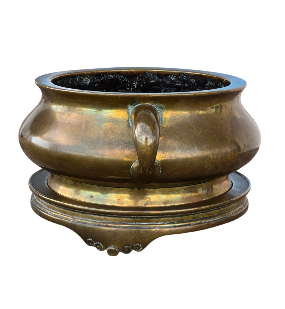A heavy Chinese bronze ritual censer featuring twin loop handles and resting on a matching fitted base with shaped feet. View II