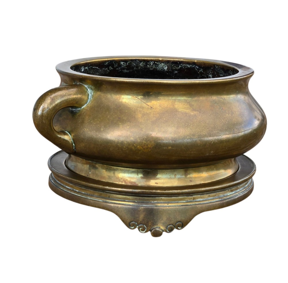 A heavy Chinese bronze ritual censer featuring twin loop handles and resting on a matching fitted base with shaped feet. View V