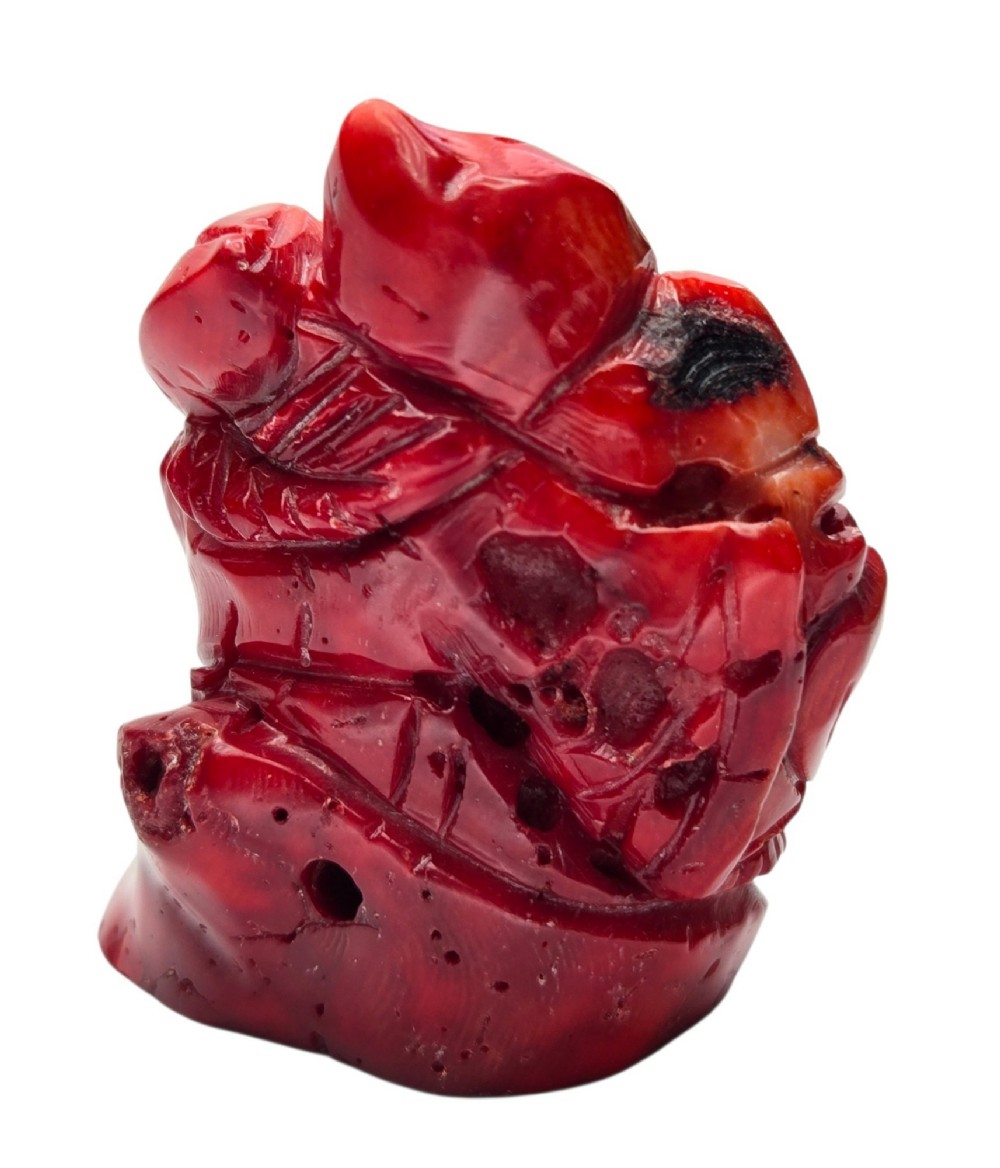A hand-carved deep red coral sculpture depicting the laughing figure of Budai following the natural shape of a coral branch. View II