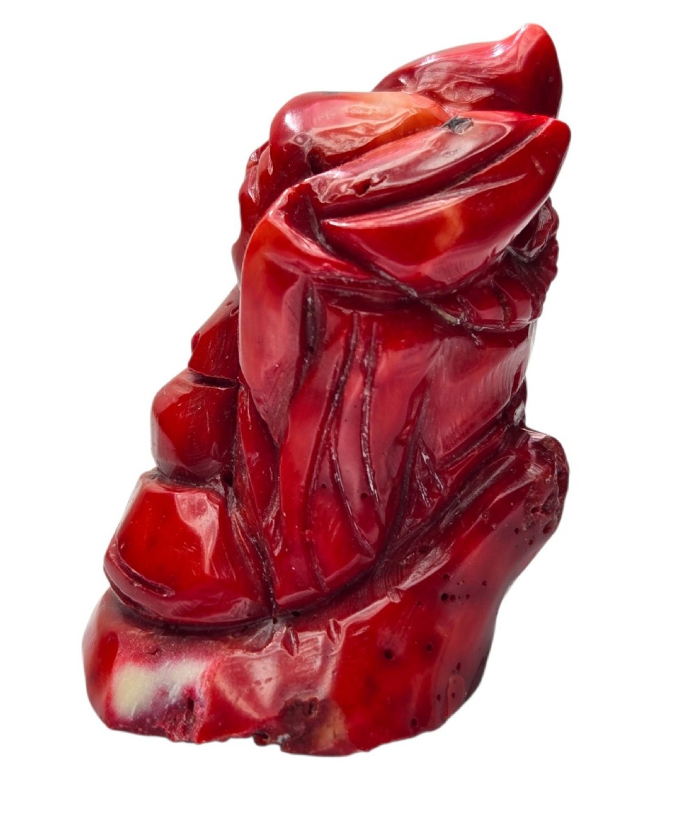 A hand-carved deep red coral sculpture depicting the laughing figure of Budai following the natural shape of a coral branch. View V