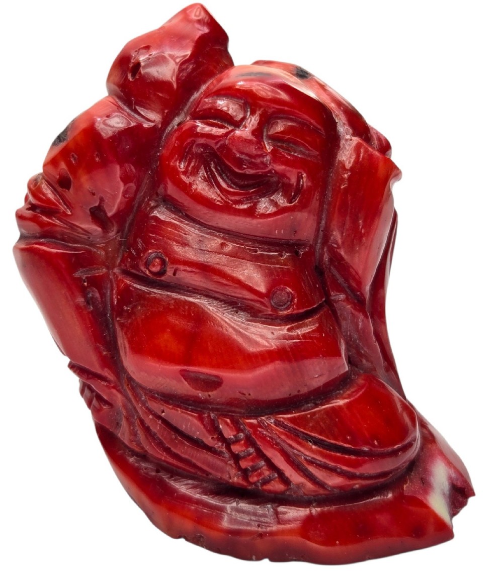 A hand-carved deep red coral sculpture depicting the laughing figure of Budai following the natural shape of a coral branch. View VIII