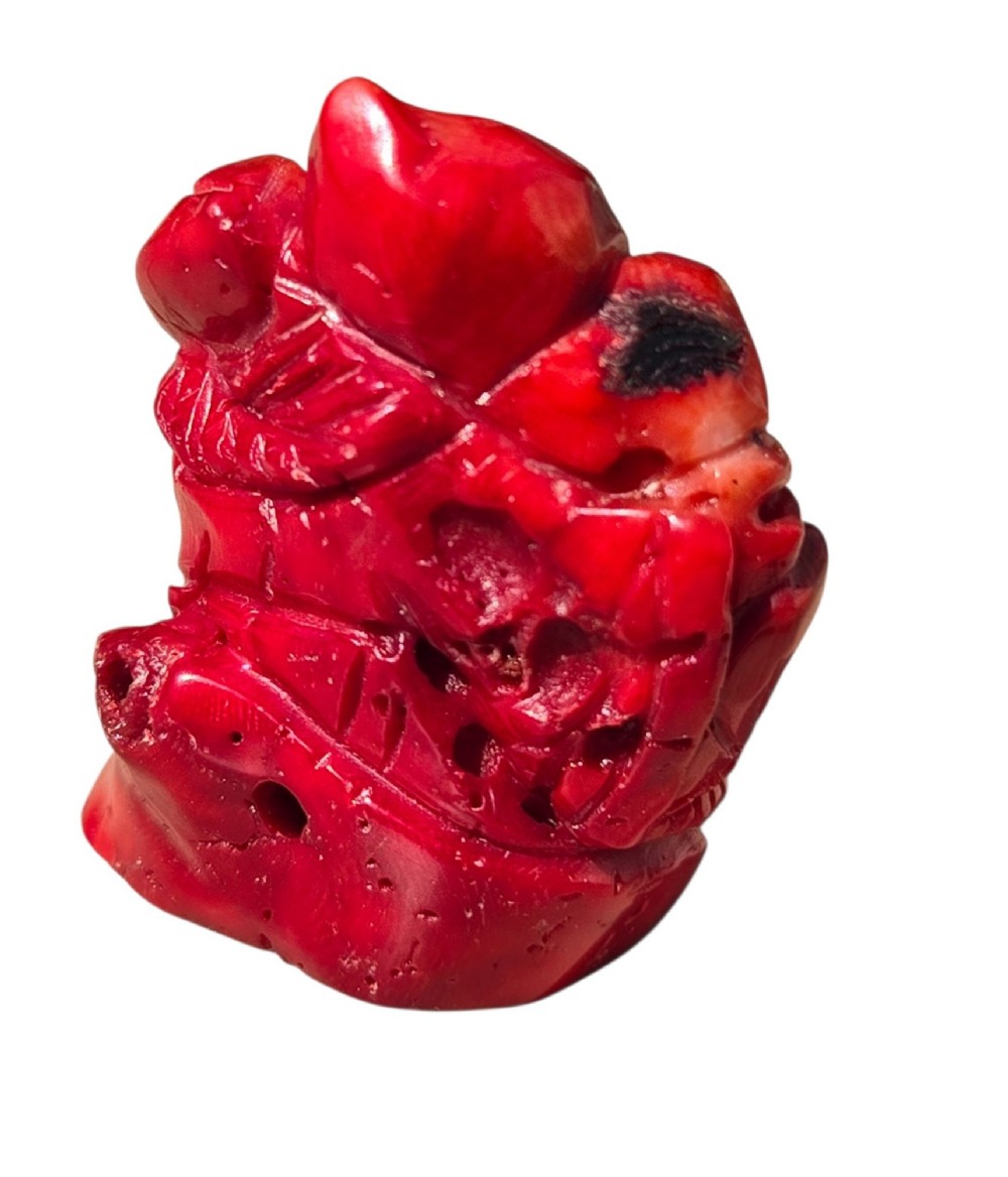 A hand-carved deep red coral sculpture depicting the laughing figure of Budai following the natural shape of a coral branch. View X