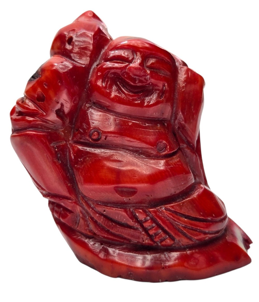 A hand-carved deep red coral sculpture depicting the laughing figure of Budai following the natural shape of a coral branch. View XII