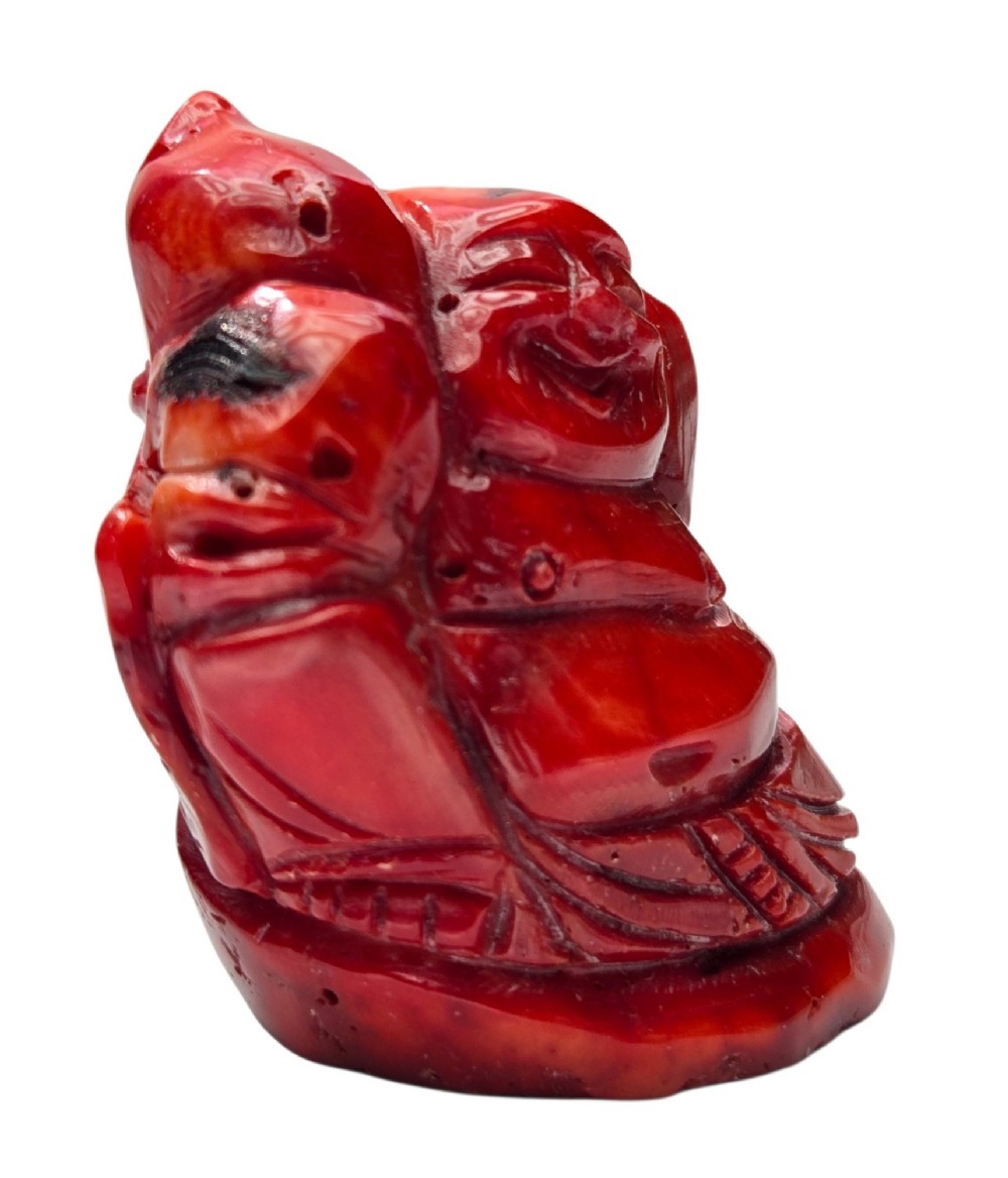A hand-carved deep red coral sculpture depicting the laughing figure of Budai following the natural shape of a coral branch. View XIII