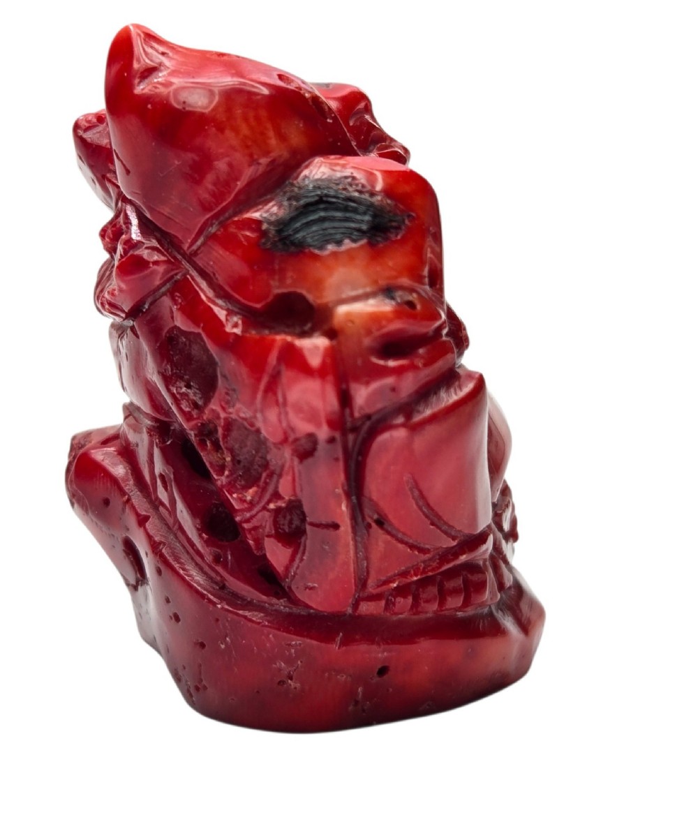 A hand-carved deep red coral sculpture depicting the laughing figure of Budai following the natural shape of a coral branch. View XIV