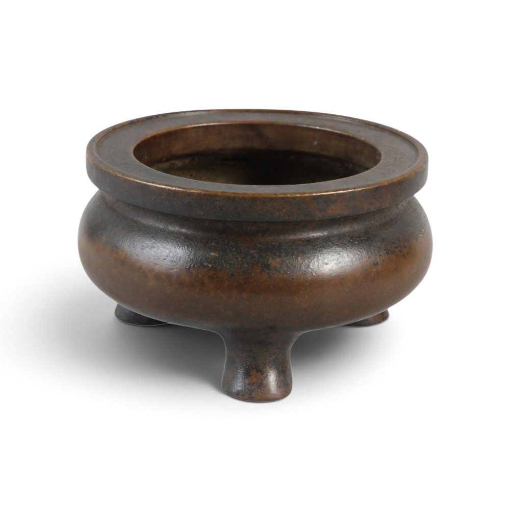 A heavy 17th-century Chinese archaistic bronze tripod censer featuring a compressed globular body, wide flat rim, dark brown patina, and three sturdy feet.