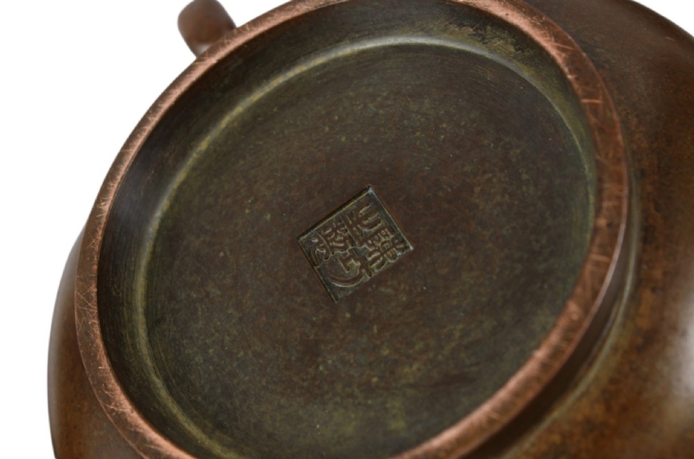 A rounded dark bronze Chinese censer with elephant head handles, topped with a polished wood lid featuring a green jade finial, resting on a carved hardwood stand. View VII