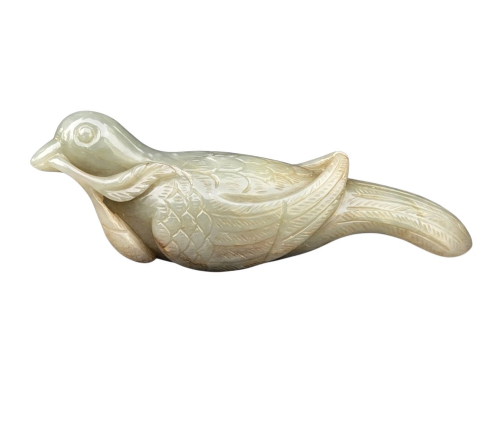 A carved celadon jade figure depicting a resting water bird holding a leafy stem in its beak.