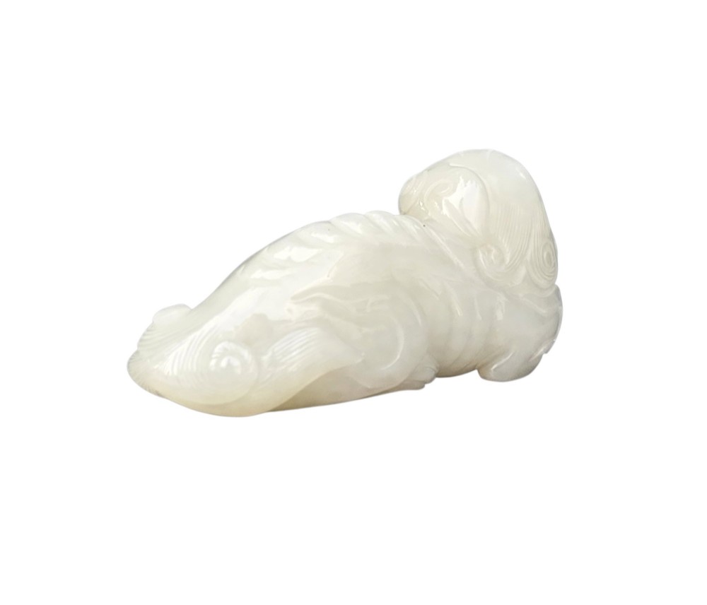 A polished white jade carving depicting a recumbent mythical beast resting on its paws with incised tail and mane details. View II
