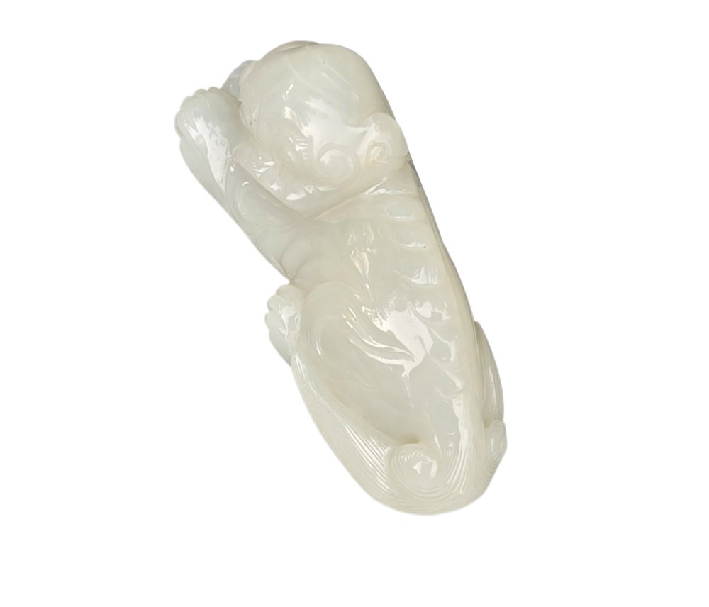 A polished white jade carving depicting a recumbent mythical beast resting on its paws with incised tail and mane details. View III