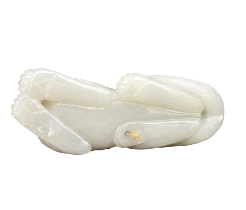 A polished white jade carving depicting a recumbent mythical beast resting on its paws with incised tail and mane details. View IV