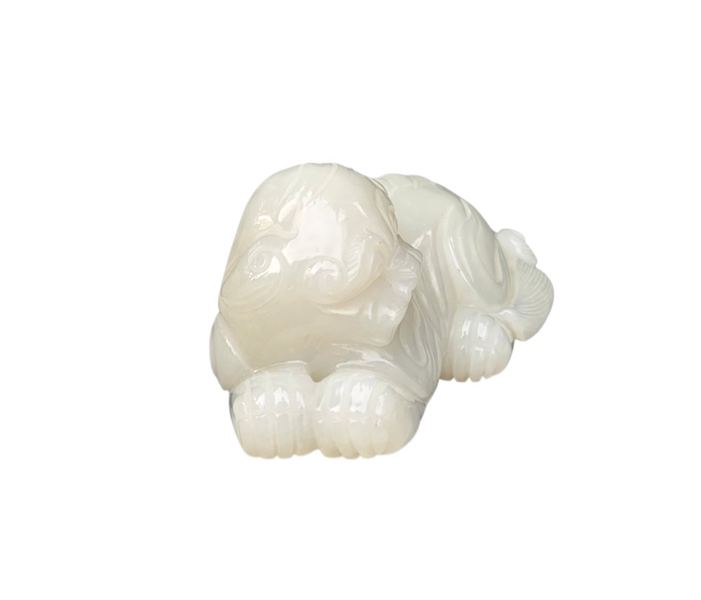 A polished white jade carving depicting a recumbent mythical beast resting on its paws with incised tail and mane details. View V