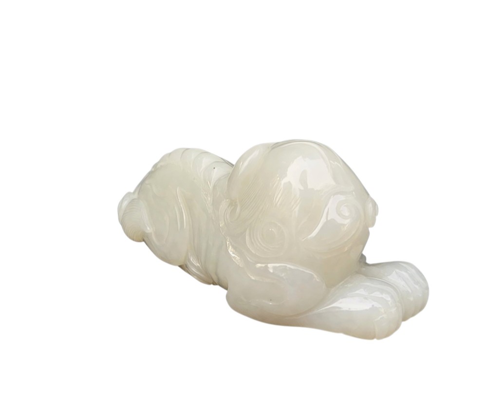 A polished white jade carving depicting a recumbent mythical beast resting on its paws with incised tail and mane details. View VI