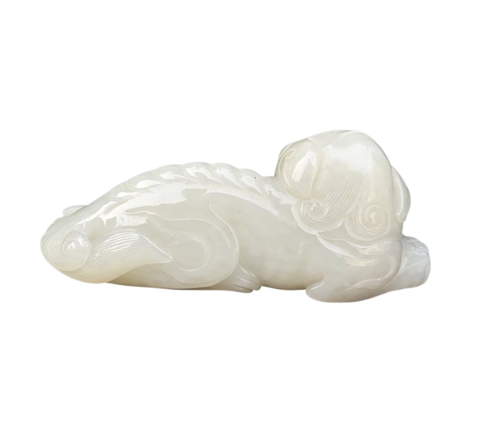 A polished white jade carving depicting a recumbent mythical beast resting on its paws with incised tail and mane details. View VII
