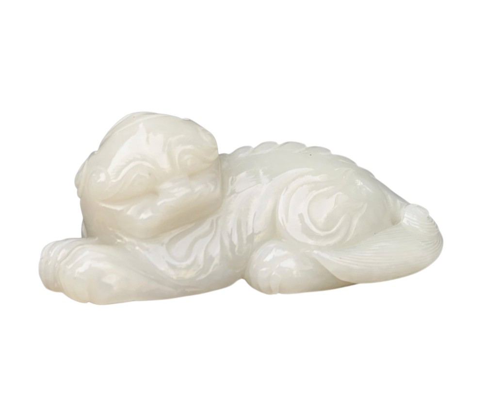 A polished white jade carving depicting a recumbent mythical beast resting on its paws with incised tail and mane details. View VIII