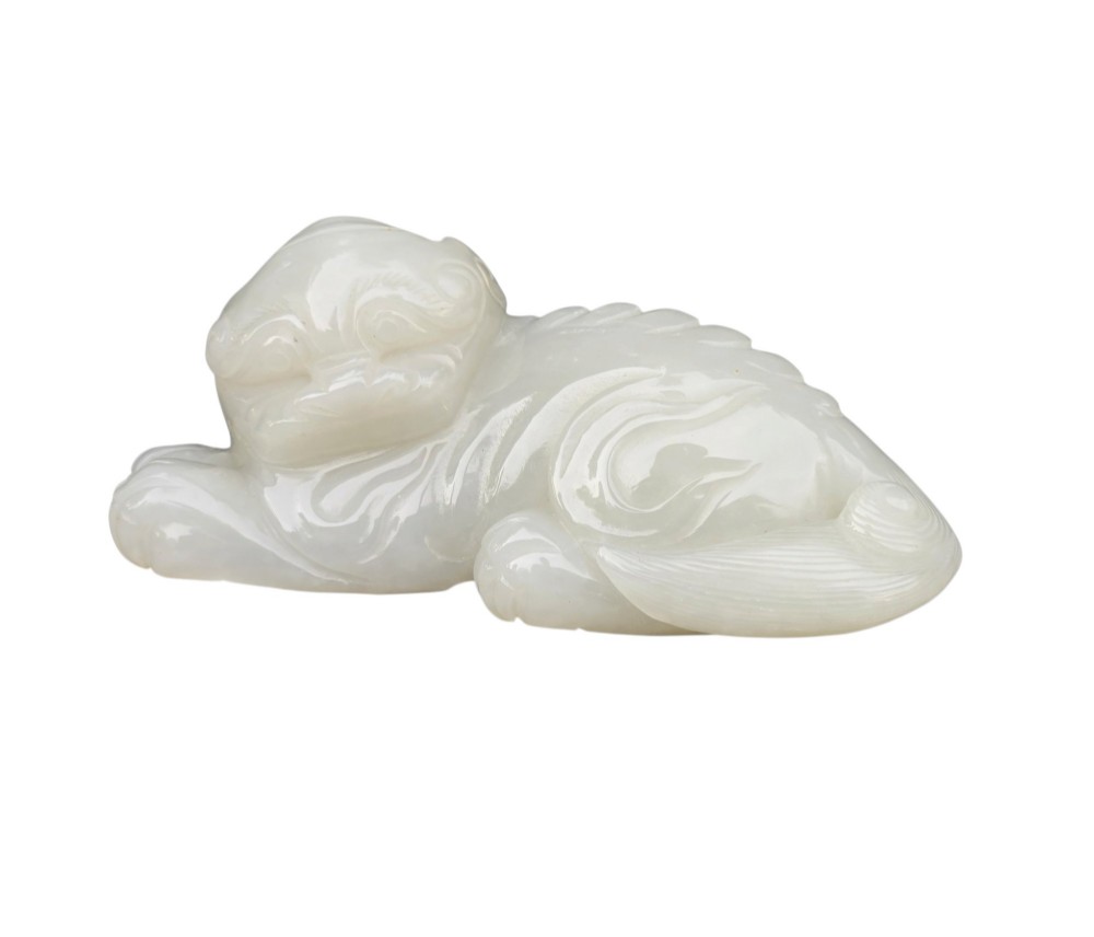 A polished white jade carving depicting a recumbent mythical beast resting on its paws with incised tail and mane details. View IX