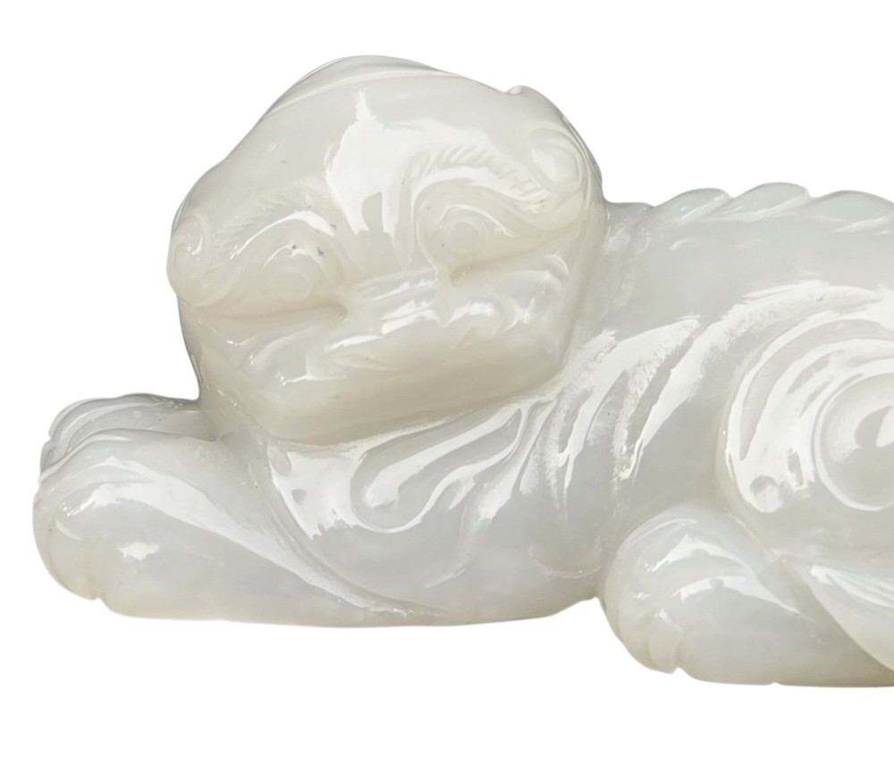 A polished white jade carving depicting a recumbent mythical beast resting on its paws with incised tail and mane details. View X