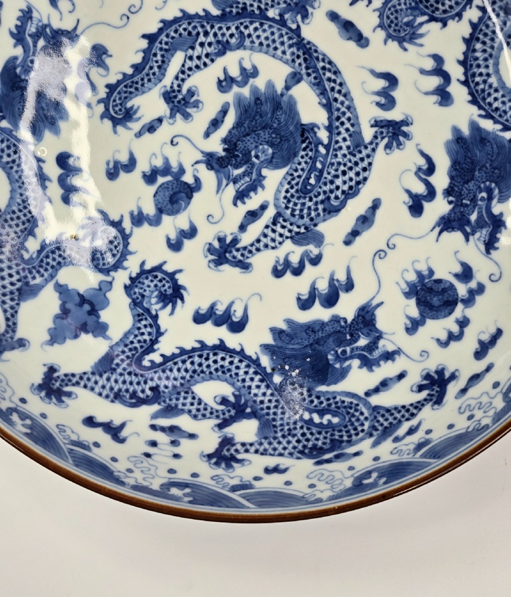 A circular Chinese blue and white porcelain charger featuring five-clawed dragons depicted among stylized clouds and flaming pearls. View IX