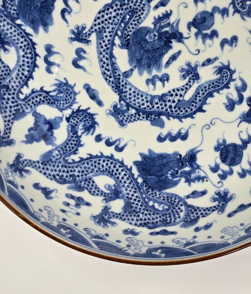 A circular Chinese blue and white porcelain charger featuring five-clawed dragons depicted among stylized clouds and flaming pearls. View X